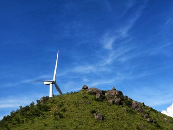 Low angle view of wind turbines on hill against blue sky