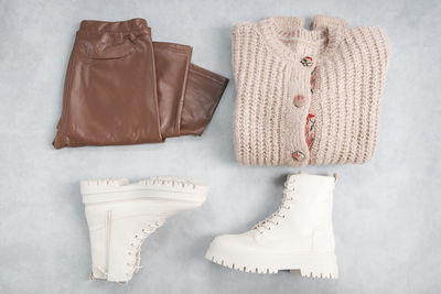 White boots made with buckles, laces, rough soles, knitted cardigan and brown leggings on a gray