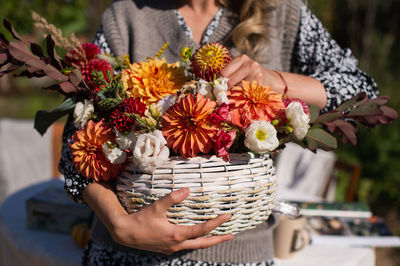 A white basket with seasonal autumn flowers dahlias and asters in her hands