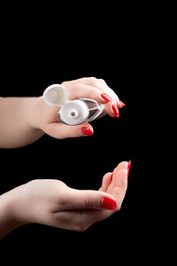 Cropped hand of woman holding bottle against black background