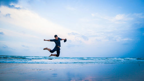 Man jumping on shore at beach against sky