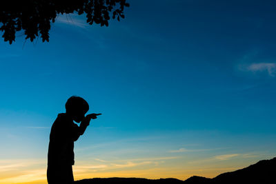 Silhouette boy gesturing while standing against blue sky