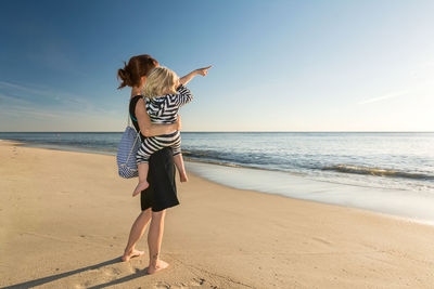 Full length of woman with daughter at beach against sky