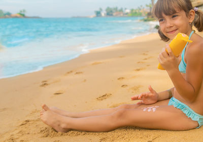 Girl with suntan lotion sitting at beach