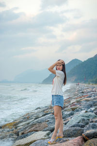 Young woman standing on rock by sea against sky