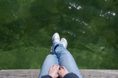 Low section of man sitting on pier over lake