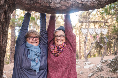 Portrait of smiling senior woman standing with friend at forest