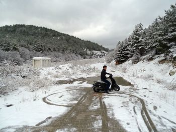 Full length of man riding motor scooter on snowy road during winter