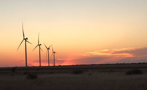 Wind turbines on field against sky during sunset