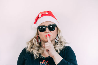 Portrait of woman wearing sunglasses while gesturing against wall