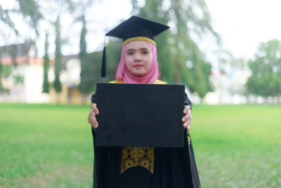 Portrait of woman holding placard on field