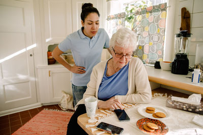 Young female volunteer looking at retired elderly woman using smart phone in nursing home