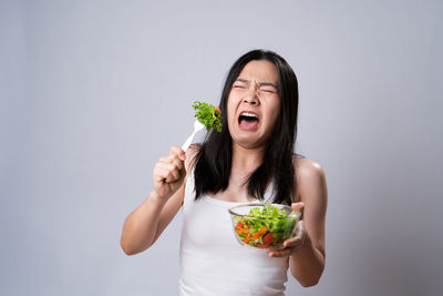 Young woman eating food against white background