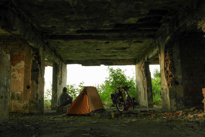 Man sitting by tent under bridge