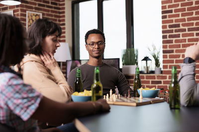 Smiling man sitting by friends playing chess at home