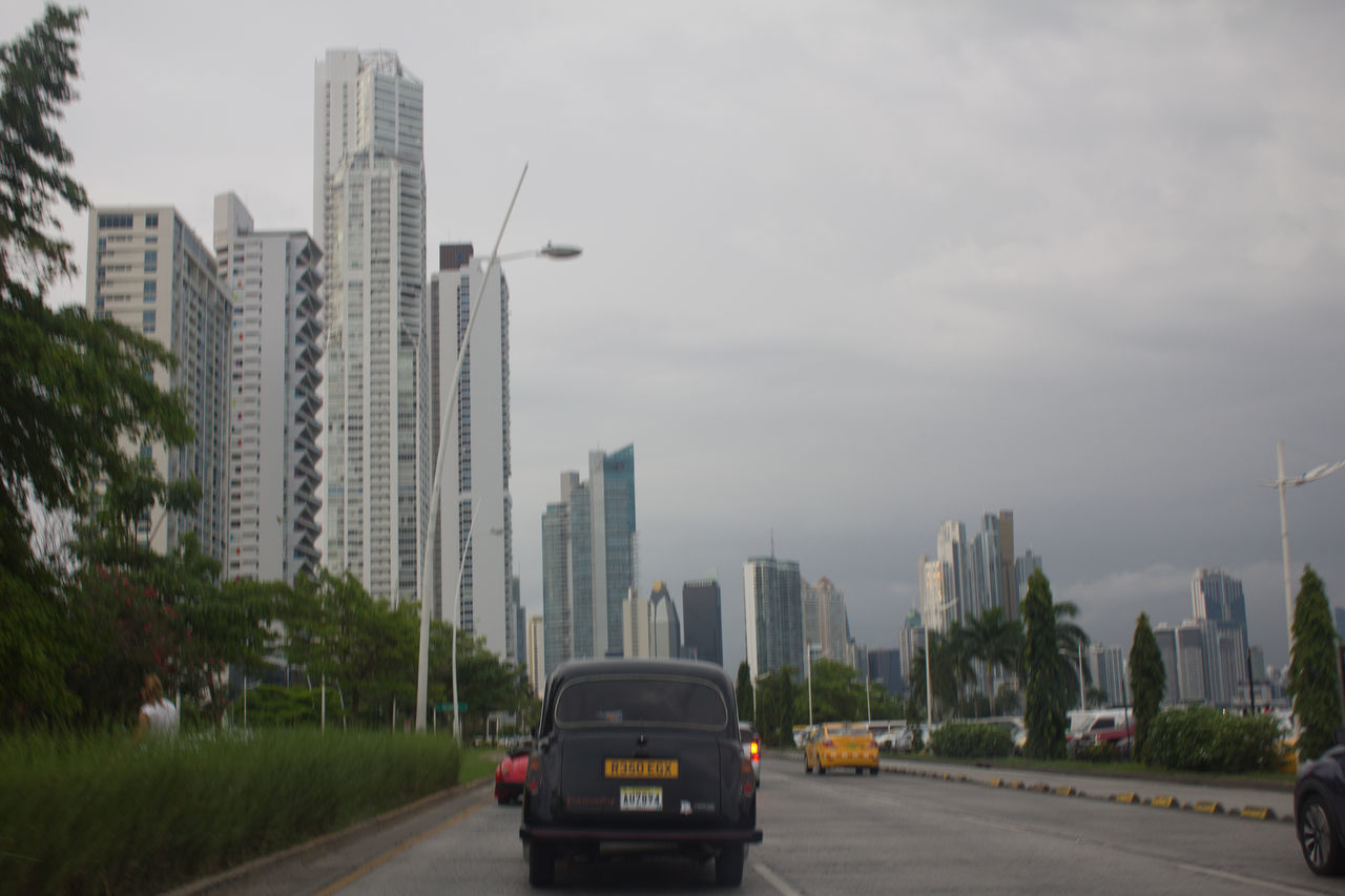 CARS ON ROAD AMIDST BUILDINGS IN CITY AGAINST SKY