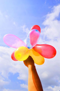 Low angle view of hand holding colorful balloons against sky