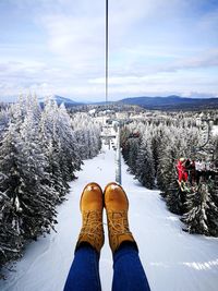 Low section of person wearing shoes over forest against cloudy sky during winter
