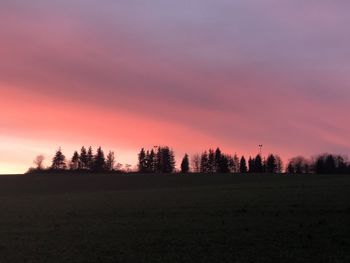 Silhouette trees on field against sky at sunset