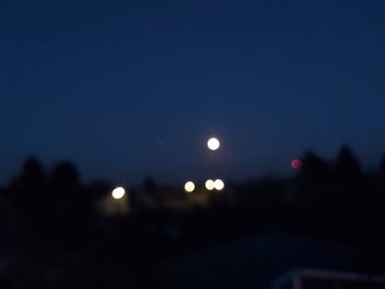 Defocused image of illuminated lights against clear sky at night