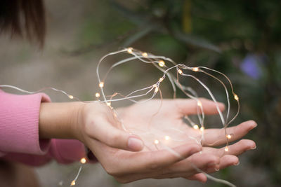 Cropped hands of woman holding illuminated string lights