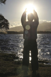 Boy standing by sea against sky during sunset