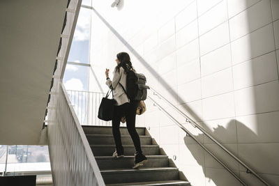 Rear view of businesswoman with backpack moving up on staircase at railroad station