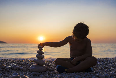 Man sitting on rocks at beach during sunset