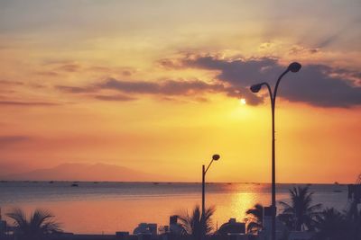 Silhouette street by sea against sky during sunset
