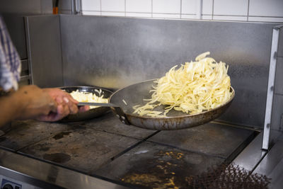 Cropped hands of chef sauteing onions in kitchen of restaurant