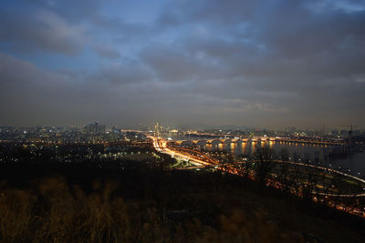 Illuminated bridge over city against cloudy sky