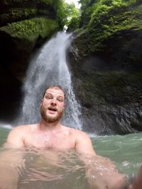 Portrait of young man standing against waterfall