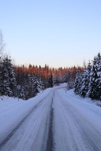 Snow covered road by trees against clear sky