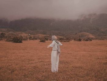 Full length of woman with arms outstretched standing on field