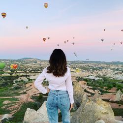 Rear view of woman looking at hot air balloons while standing on rock