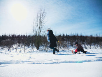 People on snowy field against sky during winter