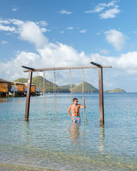 Rear view of woman swinging in sea against sky