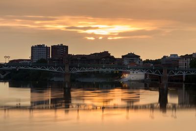 Bridge over river in city against sky during sunset