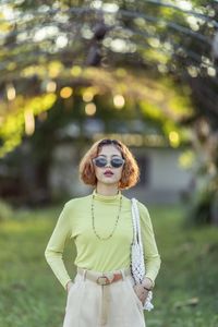 Portrait of young woman wearing sunglasses standing in park