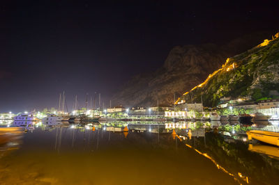 Illuminated harbor by sea against sky at night