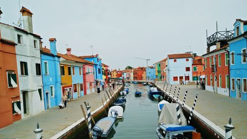 Boats moored in canal amidst houses against clear sky