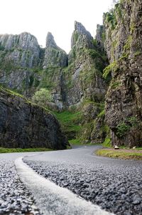 Surface level view of empty country road against rocky cliff