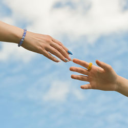 Two hands reaching out to one another, almost touching, in front of cloudy sky. help and support 