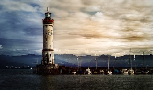 Lighthouse at harbor by sea against cloudy sky