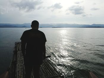 Rear view of man standing on wooden raft at sea against sky