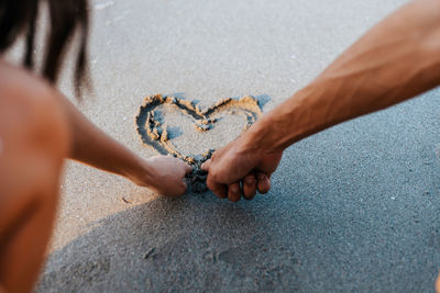 Midsection of man making heart shape on sand at beach