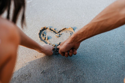 Close-up of couple hands making heart shape on sand at beach