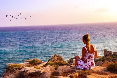 Woman sitting on beach looking at sea against sky