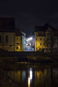 Illuminated buildings by river against sky at night