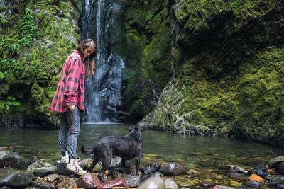 Young woman looking down at dog near waterfall